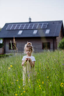 A young girl stands proudly in front of her family's solar-powered home, promoting a sustainable and eco-friendly lifestyle. - HPIF31847