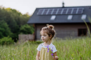 Kleines Mädchen posiert vor dem Haus der Familie, das mit Solarzellen betrieben wird, und wirbt für nachhaltiges Leben und erneuerbare Energien - HPIF31848