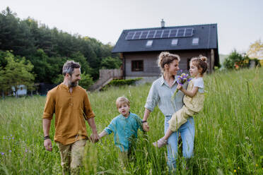 Eine fröhliche Familie posiert vor ihrem Haus, das mit Solarzellen auf dem Dach ausgestattet ist - HPIF31849