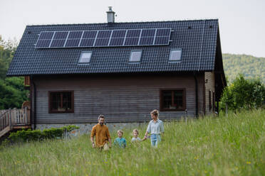 Eine fröhliche Familie posiert vor ihrem Haus und zeigt stolz ihre Solarzellen auf dem Dach - HPIF31855