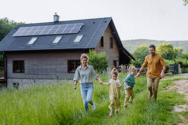 Eine fröhliche Familie posiert vor ihrem Haus, das durch Solarzellen auf dem Dach mit Strom versorgt wird - HPIF31857