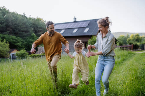 Eine Familie macht einen Spaziergang in der Nähe ihres Hauses, das mit Solarzellen auf dem Dach für nachhaltige Energie sorgt - HPIF31858