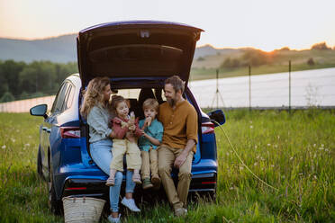 Eine fröhliche Familie wartet darauf, dass ihr Elektroauto aufgeladen wird, bevor sie sich auf ein Picknick-Abenteuer im Kofferraum einlässt - HPIF31872