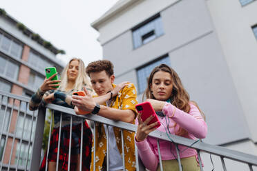 Eine Gruppe trendiger Studenten der Generation Z, die sich in der Stadt unter freiem Himmel treffen, soziale Medien nutzen und Selfies machen, um die Kraft ihrer Freundschaften zu demonstrieren - HPIF31876