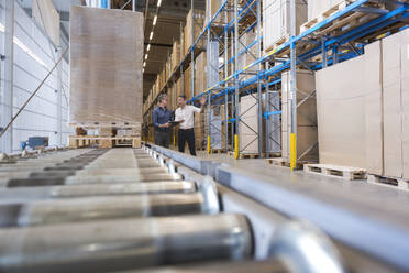 Businessmen having discussion near conveyor belt in warehouse - DIGF21004