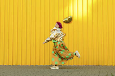 Ältere Frau, die mit einem herzförmigen Ballon vor einer gelben Wand läuft - LLUF01130