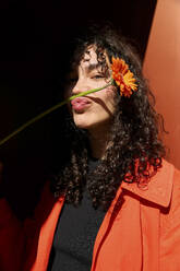 Smiling woman making puckering face with gerbera flower in front of wall - SECF00002