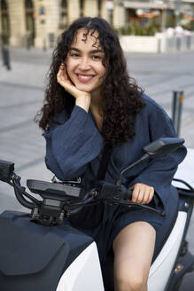 Lächelnde junge Frau auf Elektromotorroller sitzend - SECF00011