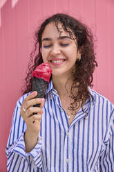 Smiling woman holding ice cream cone in front of pink wall - SECF00013