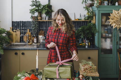 Lächelnde Frau beim Öffnen von Weihnachtsgeschenken zu Hause - VBUF00525