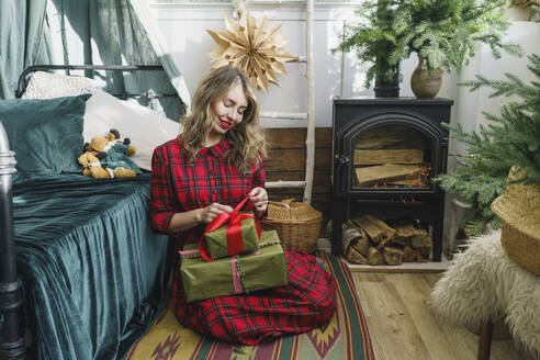Glückliche Frau beim Öffnen der Weihnachtsgeschenke zu Hause - VBUF00529