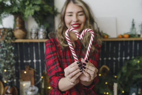 Smiling woman making heart shape with candy canes at home - VBUF00530