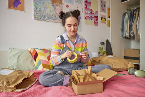 Junge Frau mit Klebeband Packung auf dem Bett zu Hause - SECF00021