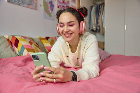 Lächelnde junge Frau hört Musik über Kopfhörer und telefoniert im Schlafzimmer - SECF00022