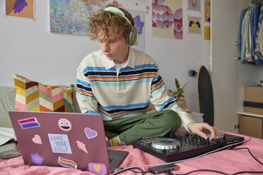 Young man with headphones using laptop and mixing sound in bedroom at home - SECF00033