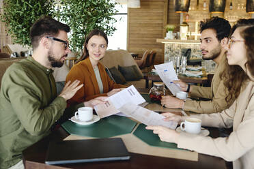 Businessman discussing over documents with colleagues at cafe - DSHF01386