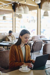 Smiling businesswoman typing on laptop at restaurant - DSHF01395