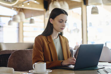 Businesswoman wearing blazer and working on laptop at restaurant - DSHF01397