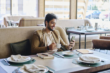Lächelnder Geschäftsmann, der über ein Smartphone im Restaurant einen Videoanruf tätigt - DSHF01400