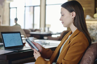 Junge Geschäftsfrau mit Smartphone in der Nähe eines Laptops im Restaurant - DSHF01401