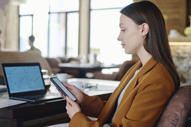 Young businesswoman using smart phone sitting near laptop at restaurant - DSHF01401