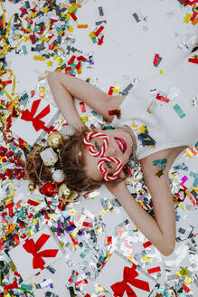 Smiling girl lying with confetti near gift boxes on white floor - MDOF01731