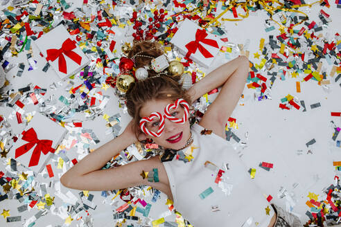 Smiling girl lying on confetti near Christmas presents - MDOF01732