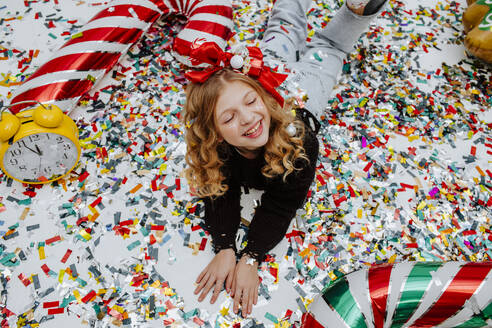 Happy girl lying on confetti with decoration at Christmas - MDOF01743