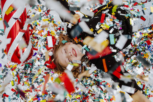 Cheerful girl lying under falling confetti on floor - MDOF01744