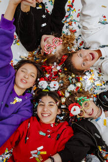 Happy friends lying near Christmas decorations on floor - MDOF01748