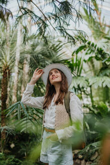 Porträt einer jungen Frau mit Hut und Rucksack im botanischen Garten, Botanikerin im Gewächshaus. - HPIF31893