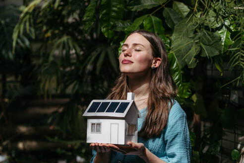 Junge Frau im Dschungel, die ein Modell eines Hauses mit Sonnenkollektoren hält, Konzept der erneuerbaren Energien und des Naturschutzes. - HPIF31908