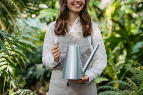 Porträt einer schönen Gärtnerin, die sich um Pflanzen im botanischen Garten kümmert. Botanikerin, Gärtnerin, die Pflanzen mit einer Gießkanne gießt. - HPIF31922