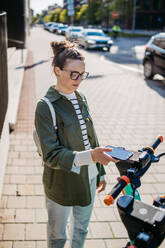 Young woman in city lending scooter with an application. E-scooter sharing system. - HPIF31954