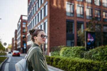 Portrait of young woman wearing glasses on city street, standing in front red brick building. - HPIF31955