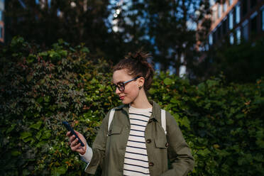 Portrait of young woman scrolling her smartphone and enjoying nature in a city park. - HPIF31956