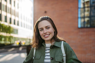 Portrait of a young woman in a city, standing in front red brick building. - HPIF31970