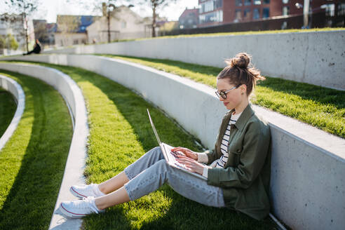 Young woman sitting in city park and working on a laptop. - HPIF31977