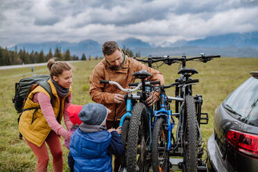 Junge Familie mit kleinen Kindern, die sich auf eine Fahrradtour in der Natur vorbereitet, indem sie die Fahrräder von den Autoträgern abstellt. Konzept der gesunden Lebensweise und der Bewegung. - HPIF32084