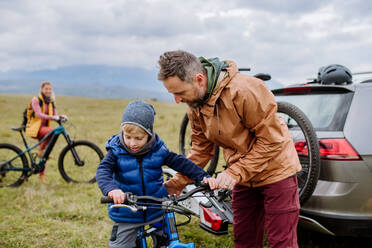 Junge Familie mit kleinen Kindern, die sich auf eine Fahrradtour in der Natur vorbereitet, indem sie die Fahrräder von den Autoträgern abstellt. Konzept der gesunden Lebensweise und der Bewegung. - HPIF32088