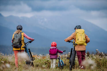 Rückansicht einer Familie mit kleinem Kind auf Fahrrädern, inmitten der herbstlichen Natur, Konzept der gesunden Lebensweise. - HPIF32094