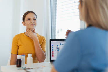 Ein Mädchen im Teenageralter schildert dem Arzt in der Klinik ihre Symptome und Schmerzen. Das Mädchen hat Halsschmerzen, Husten und Schmerzen beim Schlucken. - HPIF32123