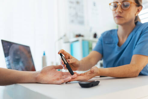 Diabetologe Arzt testet Blutprobe auf Blutzuckermessgerät in Diabetes-Klinik. Arzt nimmt Blutprobe aus dem Finger eines Jungen. Pädiatrische Diabetes in Teenager-Junge, junger Mann. - HPIF32146