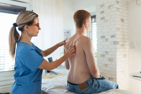 An orthopedist examines the spine, posture, and spinal deformities of a teenage patient. Teenage boy visiting paediatrician for annual preventive physical examination. Concept of preventive health care for adolescents. - HPIF32149