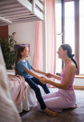 Mother waking her daughter up for school in the morning. She kneeling by the child's bed and holding her adorable daughter by hands. - HPIF32156