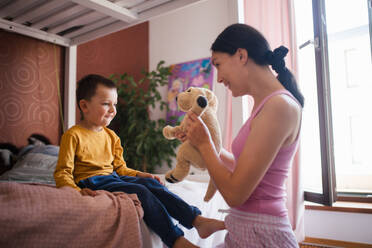 A single mother waking her son up for kindergarten in the morning. Beautiful mom awakens the preschooler with a stuffed toy, playing and making him laugh. - HPIF32157