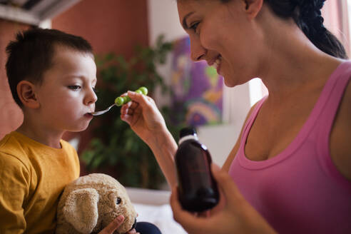 Young beautiful mother giving medicines, coughing syrup from spoon to her sick little son. Concept of children seasonal illness, viruses and kid's immune system. - HPIF32161