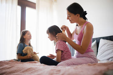 Porträt einer Mutter mit zwei Töchtern auf einem Bett im Schlafzimmer. Die Mutter kämmt die langen Haare ihrer Tochter mit einem Kamm. Konzept des Muttertags und der mütterlichen Liebe. - HPIF32162