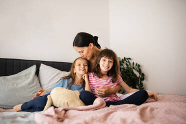 Portrait of a mother with two daughters on a bed in the bedroom. Fatherless family sit and hug each other. Concept of Mother's Day and maternal love. - HPIF32166