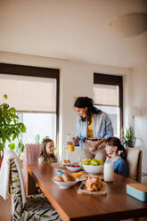 Mother prepares breakfast and pouring juice for the children, in the morning. Maternal love and care for the household and family. - HPIF32174